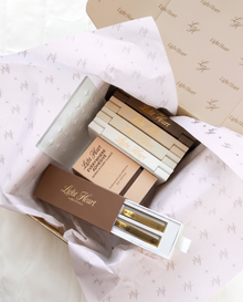 Light Heart Lashes unboxing flat lay showing the Bestie Duo tweezer set with Katy and Maddi tweezers, stacked lash trays, Everywhere Adhesive, and branded LH tissue paper inside an open Light Heart shipping box