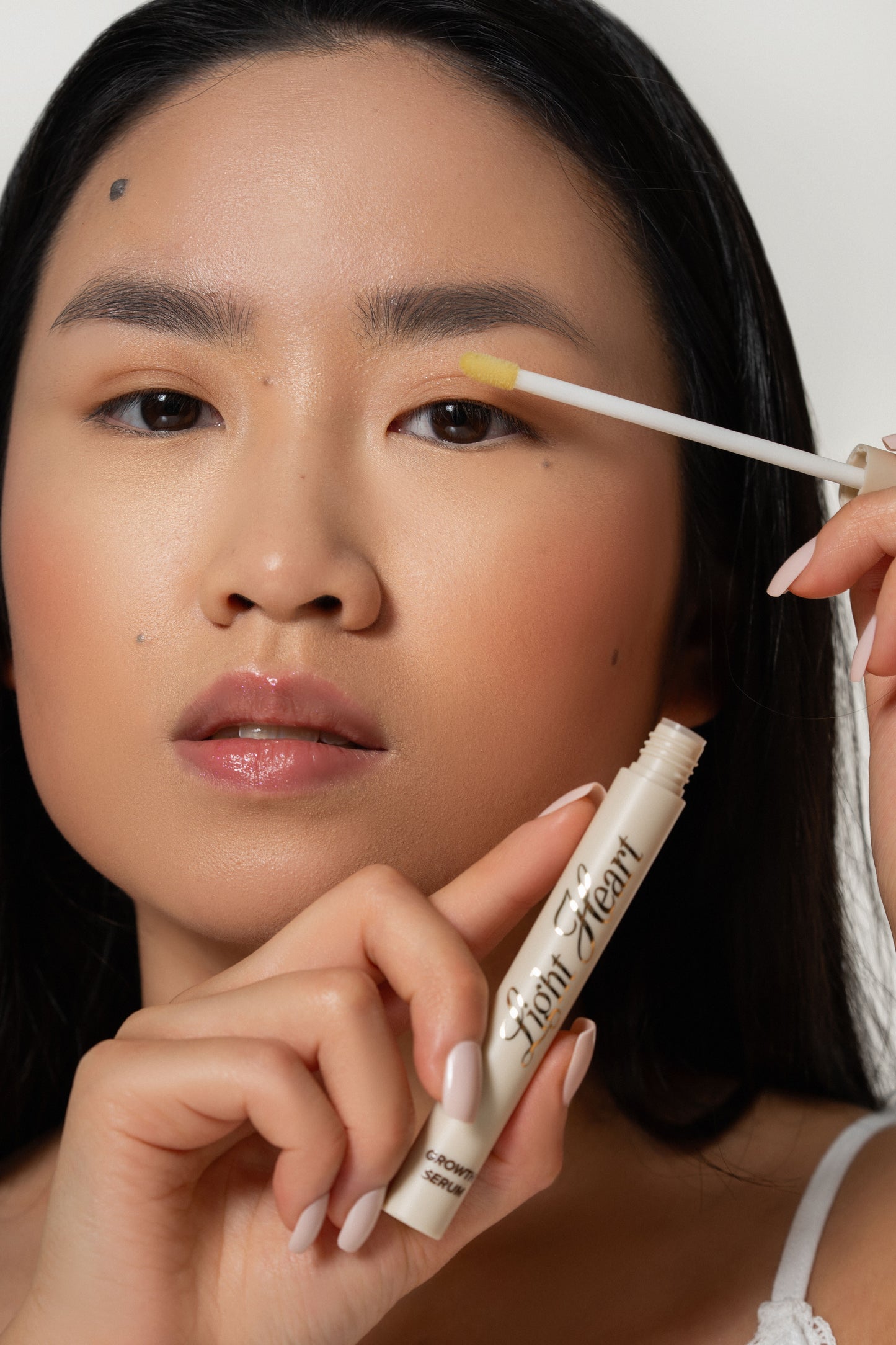 Woman applying eyebrow growth serum with applicator wand to promote fuller, thicker, healthier brows.