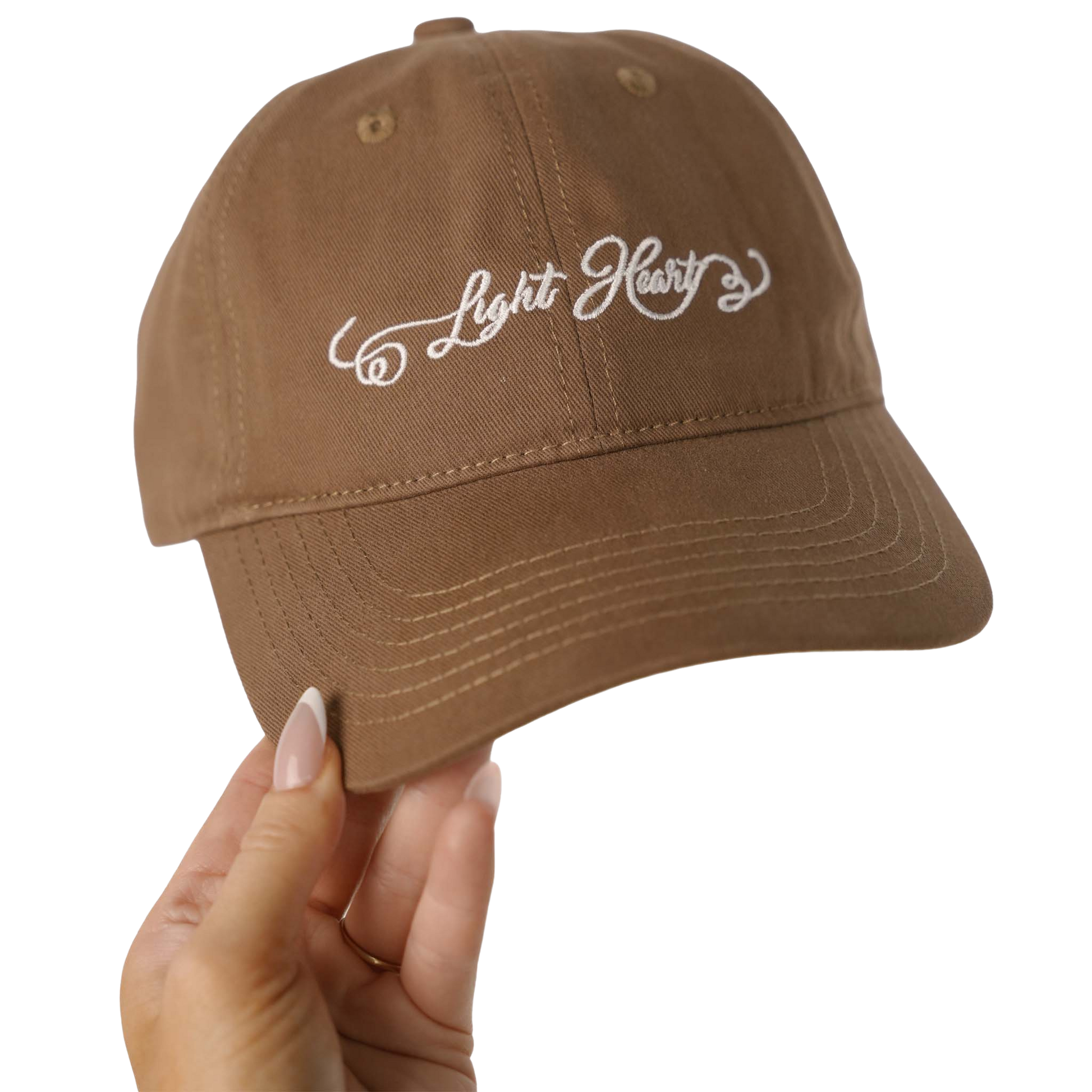 Light Heart Lashes brown dad hat with white embroidered script logo, held up by hand